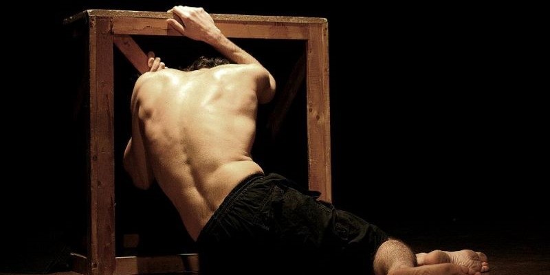 Theatrical scene: man bent over a piece of wood